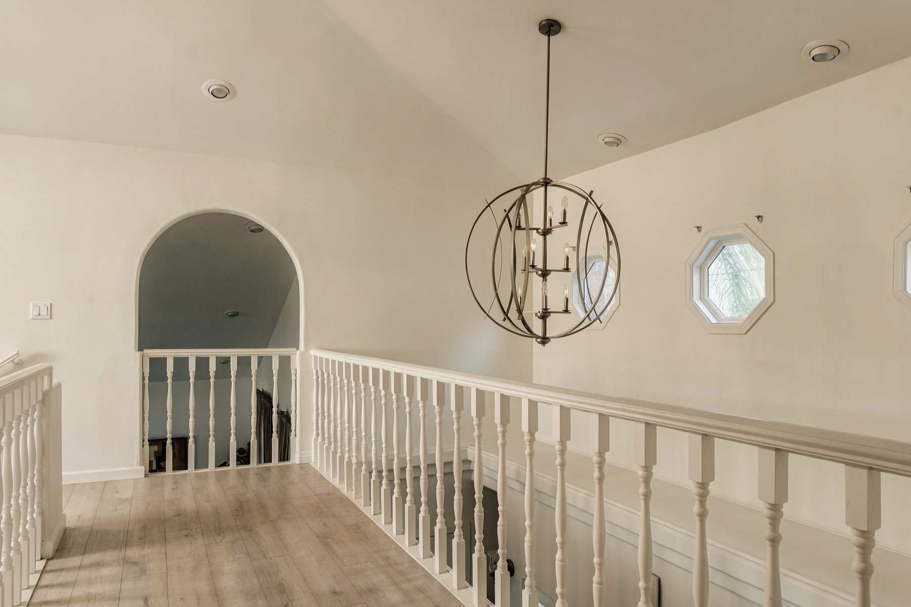 Upstairs landing with an arched passage, octagonal windows, and a ring chandelier